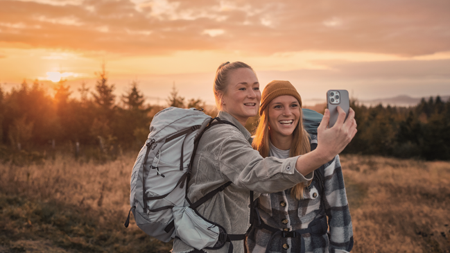 Zwei Wanderinnen machen ein Selfie zusammen vor einem Sonnenaufgang 
