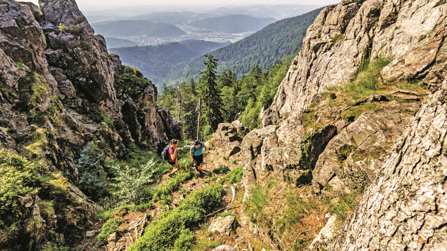 Zwei Wanderer laufen zwischen großen Felsformationen einen Berg hinauf