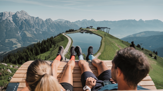 Zwei Personen sitzen auf einer Bank und genießen ein Bergpanorama