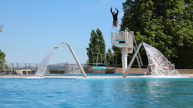 Person springt in Freibad von Sprungturm