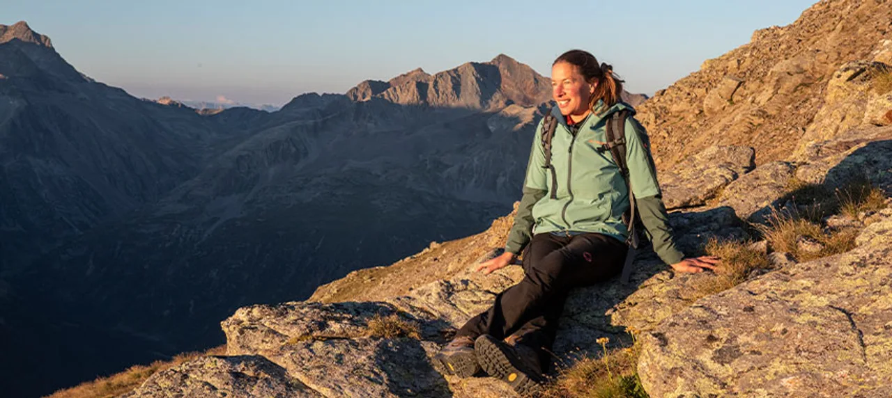 Wanderin sitzend auf Felsen in goldenem Licht während der Abendstimmung mit Blick in die Ferne.