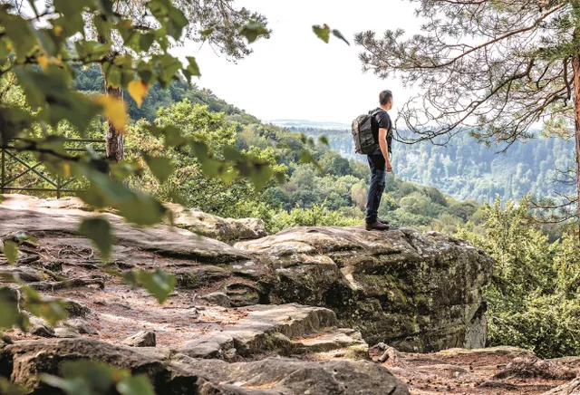 Mann steht auf einer Steinplattform am Berg und schaut ins Tal