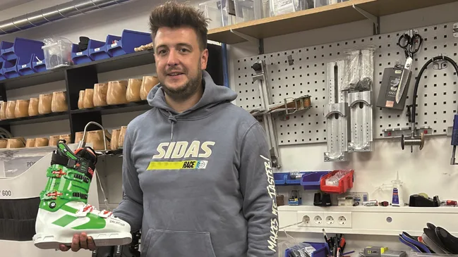 Janik Schettel steht in seiner Werkstatt und zeigt einen Skischuh