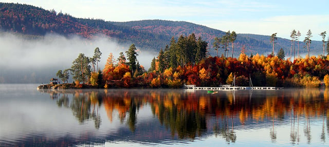 Gewässer und herbstliche Bäume vor Bergen.