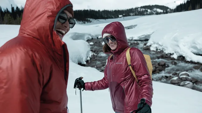 Zwei Personen neben einem Gewässer in einer verschneiten Winterlandschaft.