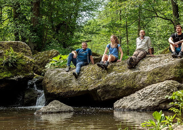 Menschen sitzend auf einem Felsen in einer Bachlandschaft im Grünen