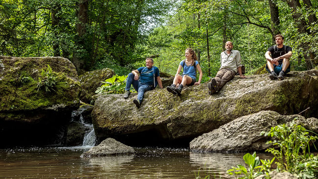 Menschen sitzend auf einem Felsen in einer Bachlandschaft im Grünen