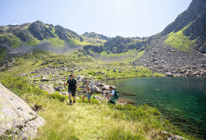 Drei Personen wandern an einem klaren Bergsee entlang
