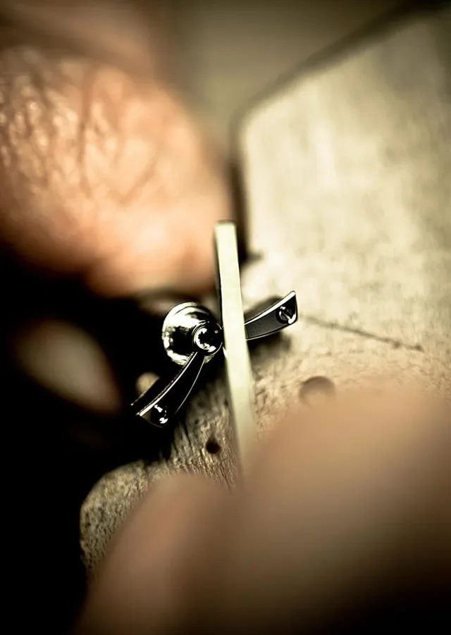 Mit einer feinen Feile wird die Komponente eines Uhrwerks angliert, also auf 45 Grad bei exakt gleichbleibender Breite abgeschrägt und poliert