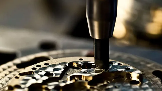 Ein kleiner Schleifkopf wird von Hand kurz auf ein Werkstück gedrückt, um es mit dicht beieinanderliegenden Kreisen, der Perlage, zu dekorieren