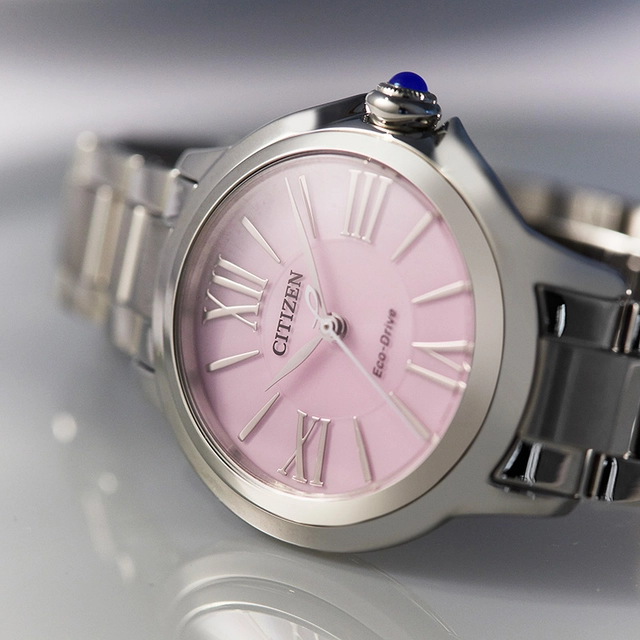 Citizen L, Referenz 241224_EM1160-58X rosa Zifferblatt, Uhr liegend vor grauem Hintergrund