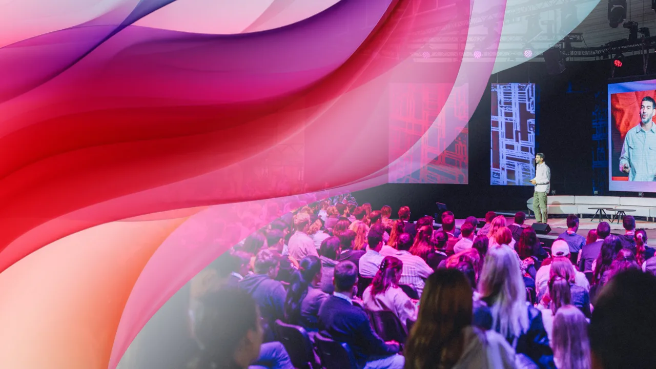 Konferenzszene mit Publikum vor einer Bühne, auf der ein Redner steht; darüber legt sich eine abstrakte, farbige Wellen-Grafik in Pink-, Rot- und Lilatönen.